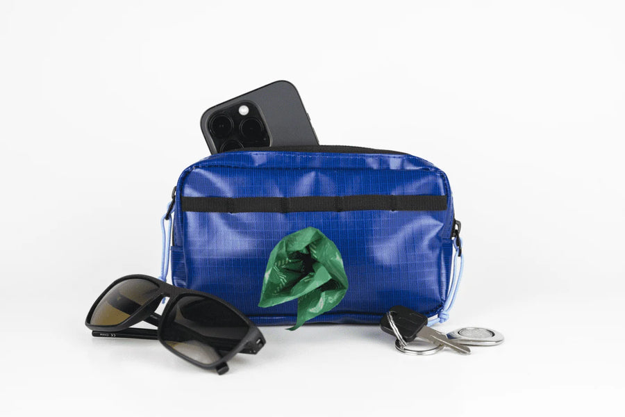 Blue Phone Pouch with built-in poop bag dispenser, holding a phone, keys, and sunglasses.