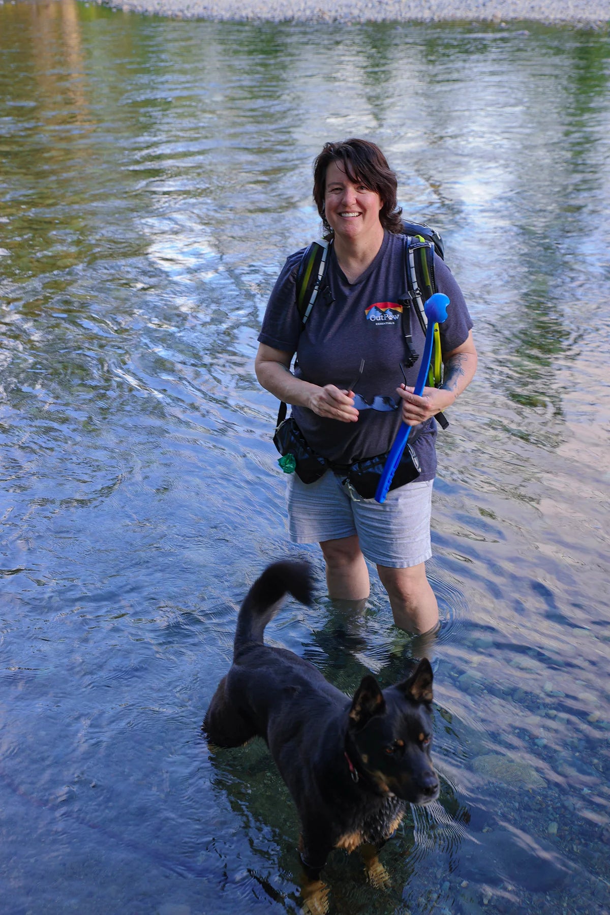 Wolf Woman Essentials founder Jennifer hiking through shallow river with loyal dog exploring backcountry wilderness terrain