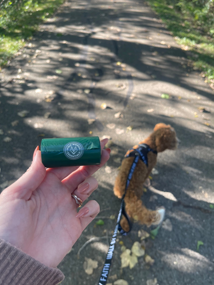 Eco Poop Bags green roll held up on a shaded trail while a customer's goldendoodle puppy walks ahead on leash