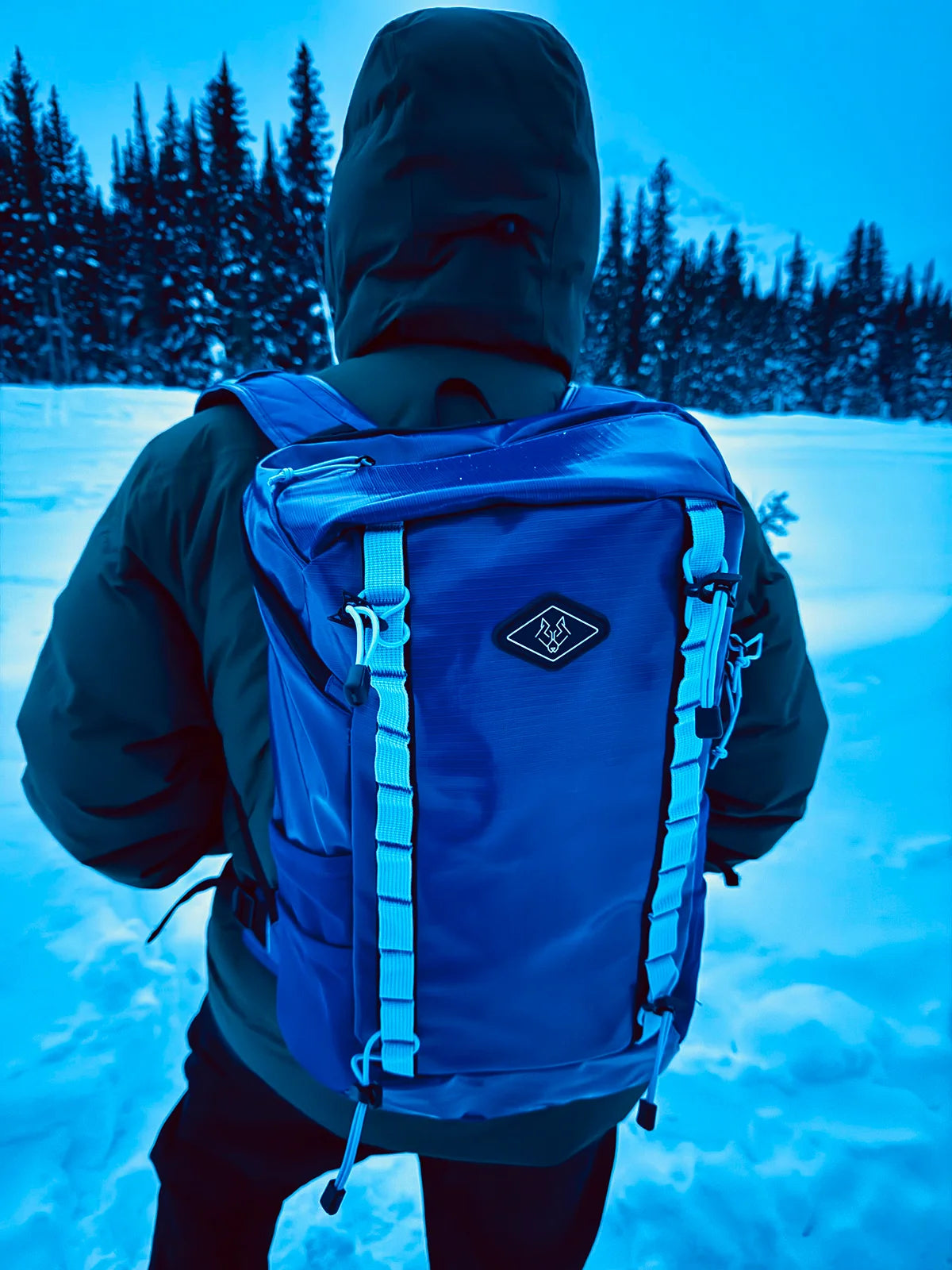 Hiker carrying rugged blue adventure backpack through deep snow in remote winter landscape