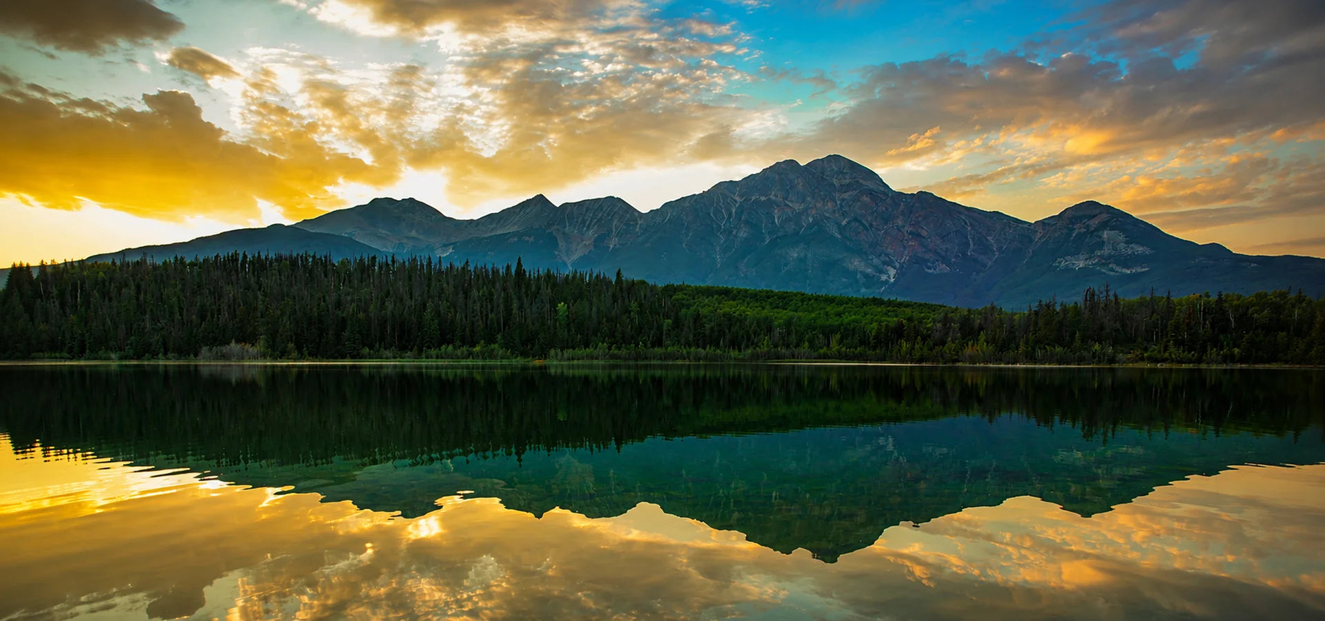 Golden sunset reflecting on calm mountain lake surrounded by pine trees — Wolf Woman Essentials protecting wild places banner